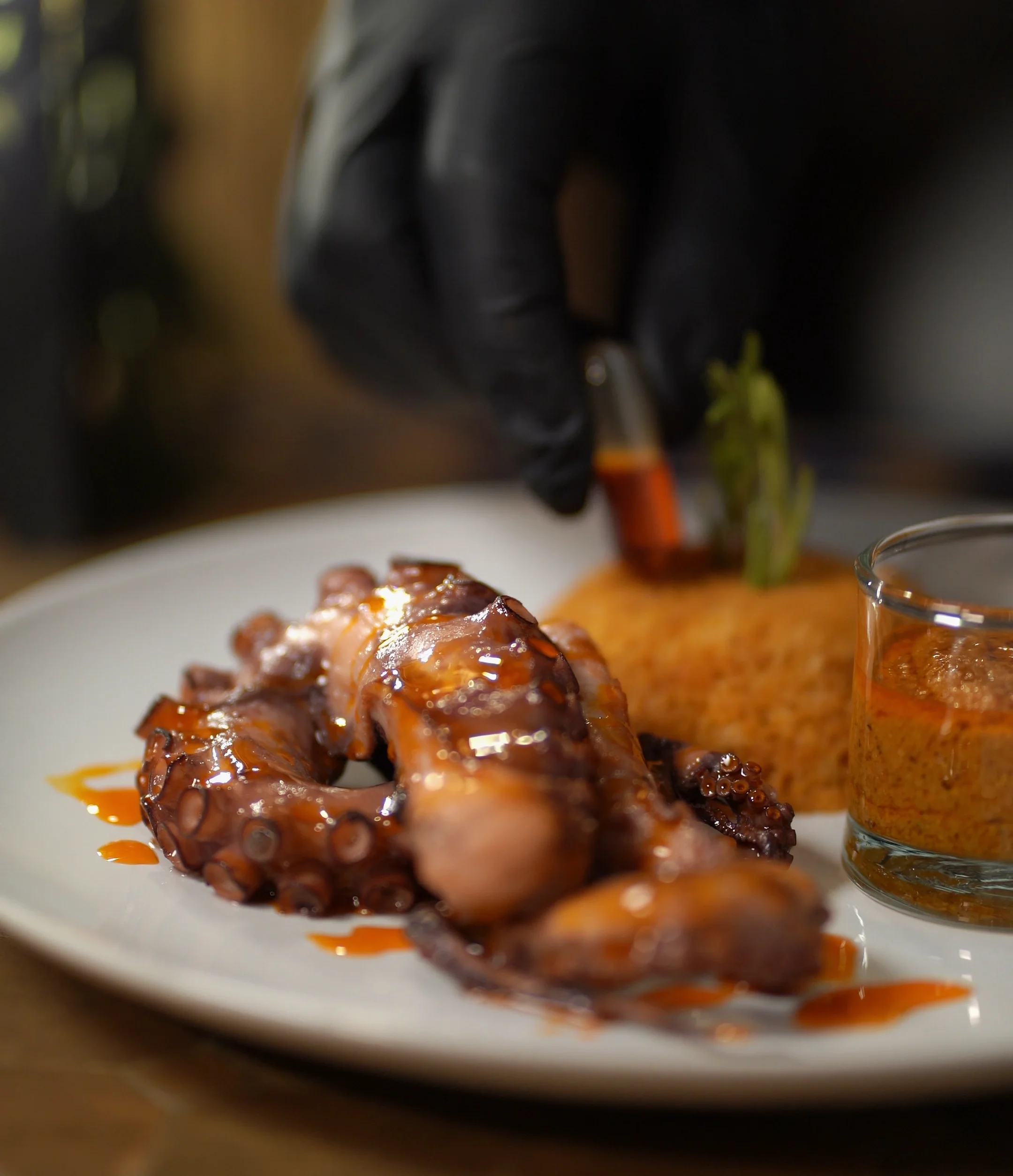 Glazed octopus plated with rice and a side of sauce