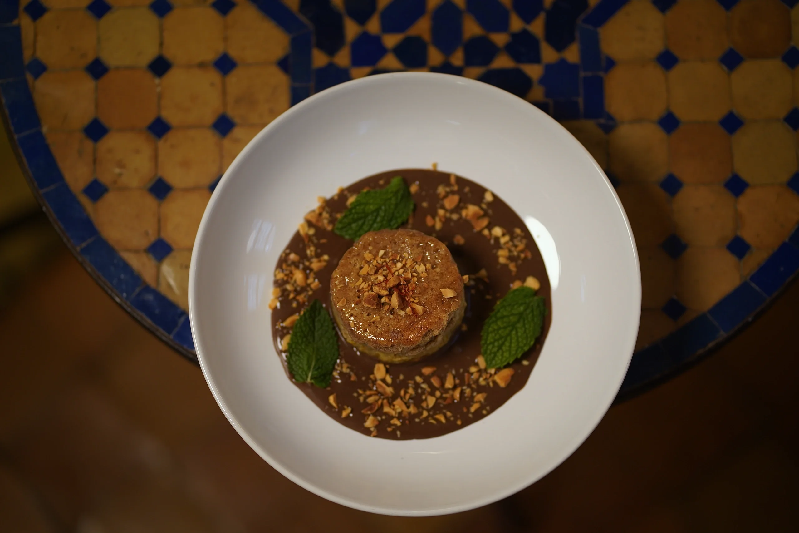 Overhead view of a dessert with chocolate sauce, toasted nuts, and mint leaves