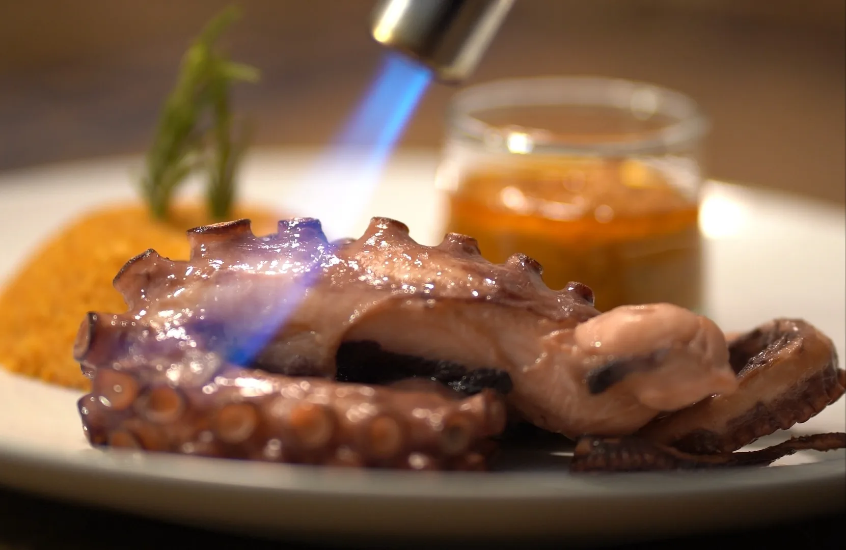 Pulpo flambeado con soplete junto a una salsa dorada