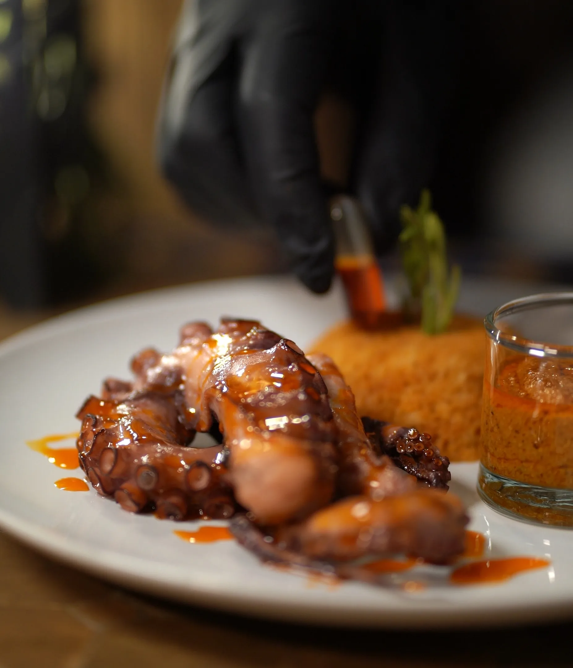 Pulpo glaseado emplatado junto a arroz y una copa de salsa